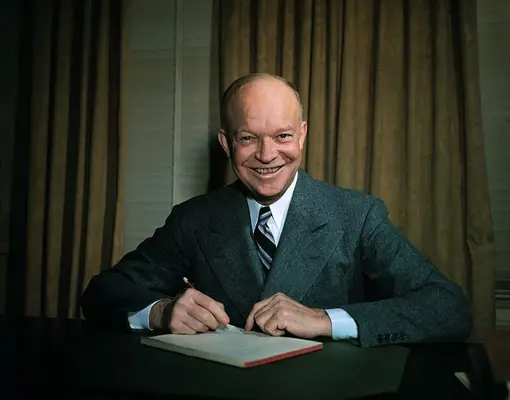 Dwight Eisenhower seated at desk with pen in hand.