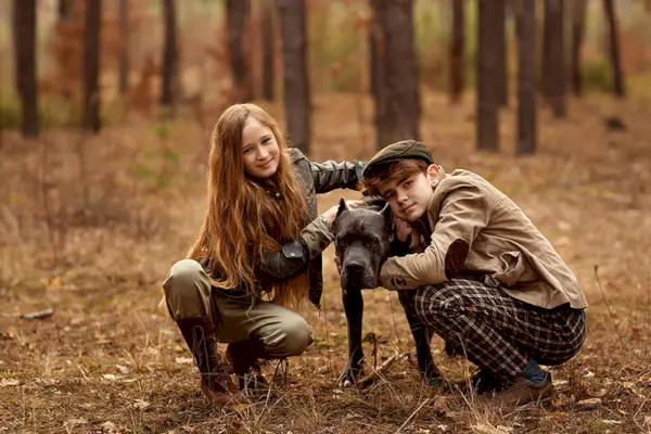 Niña y niño caminan con un perro Cane corso en el bosque y se divierten. Los niños abrazan a un perro.