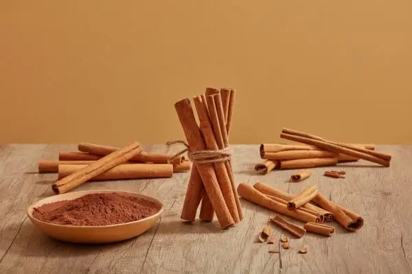 škoricové tyčinky sú zdobené na drevenom stole škoricovým práškom položeným na miske