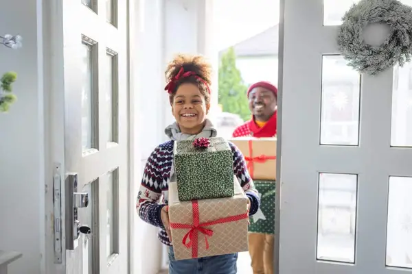 Guests entering home and holding pile of gifts for Kwanzaa.