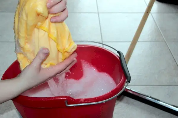 Osoba máchající mycí hadřík v kbelíku