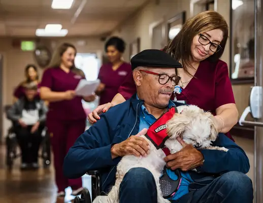 Nurse assisting senior man in wheelchair holding service dog