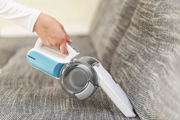 Una mujer aspirando muebles en una casa con una aspiradora portátil.