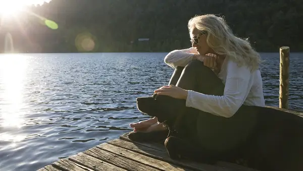 Woman pats dog on lake pier, sunrise